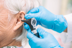 Audiologist or ENT doctor use otoscope checking ear of asian senior woman patient treating hearing loss problem.